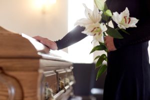 Woman Holding Flowers Standing Next To A Casket