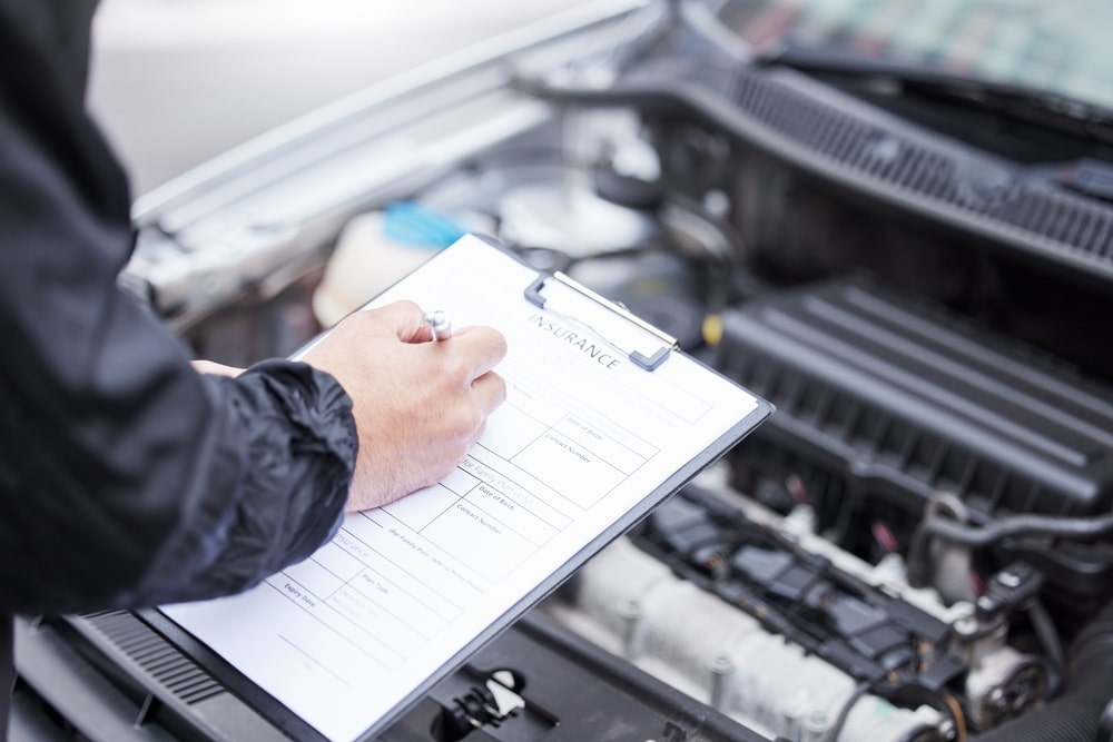 Person Filling Out Insurance Papers Looking At A Cars Engine