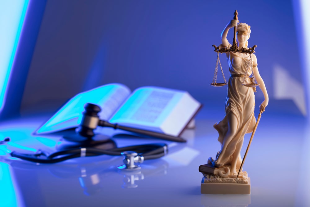 Statue Of The Lady Of Justice And A Stethoscope With Judges Hammer In The Background