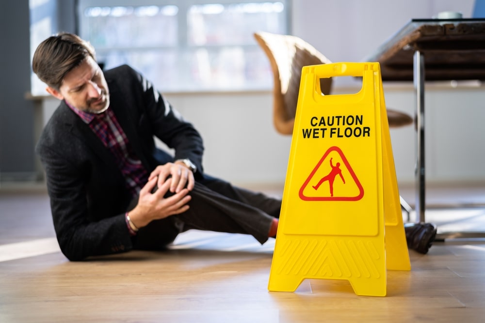 Man On The Floor Holding His Knee Next To A Wet Floor Sign