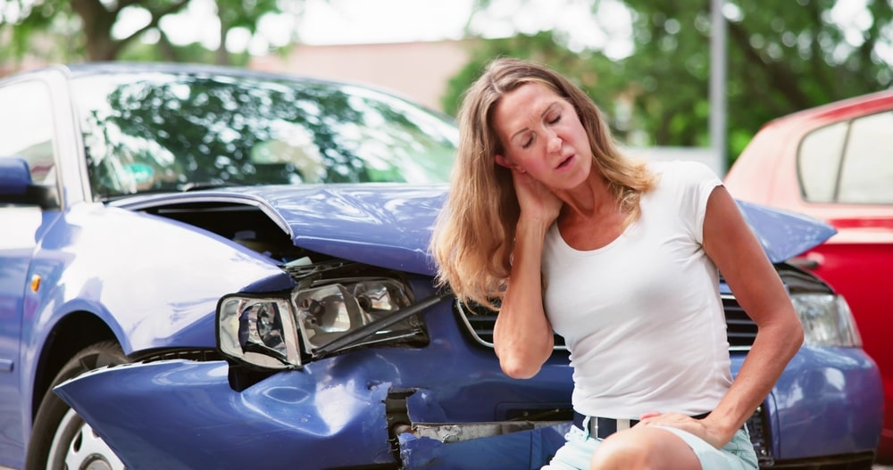 Woman Holding Her Neck Next To A Damaged Car